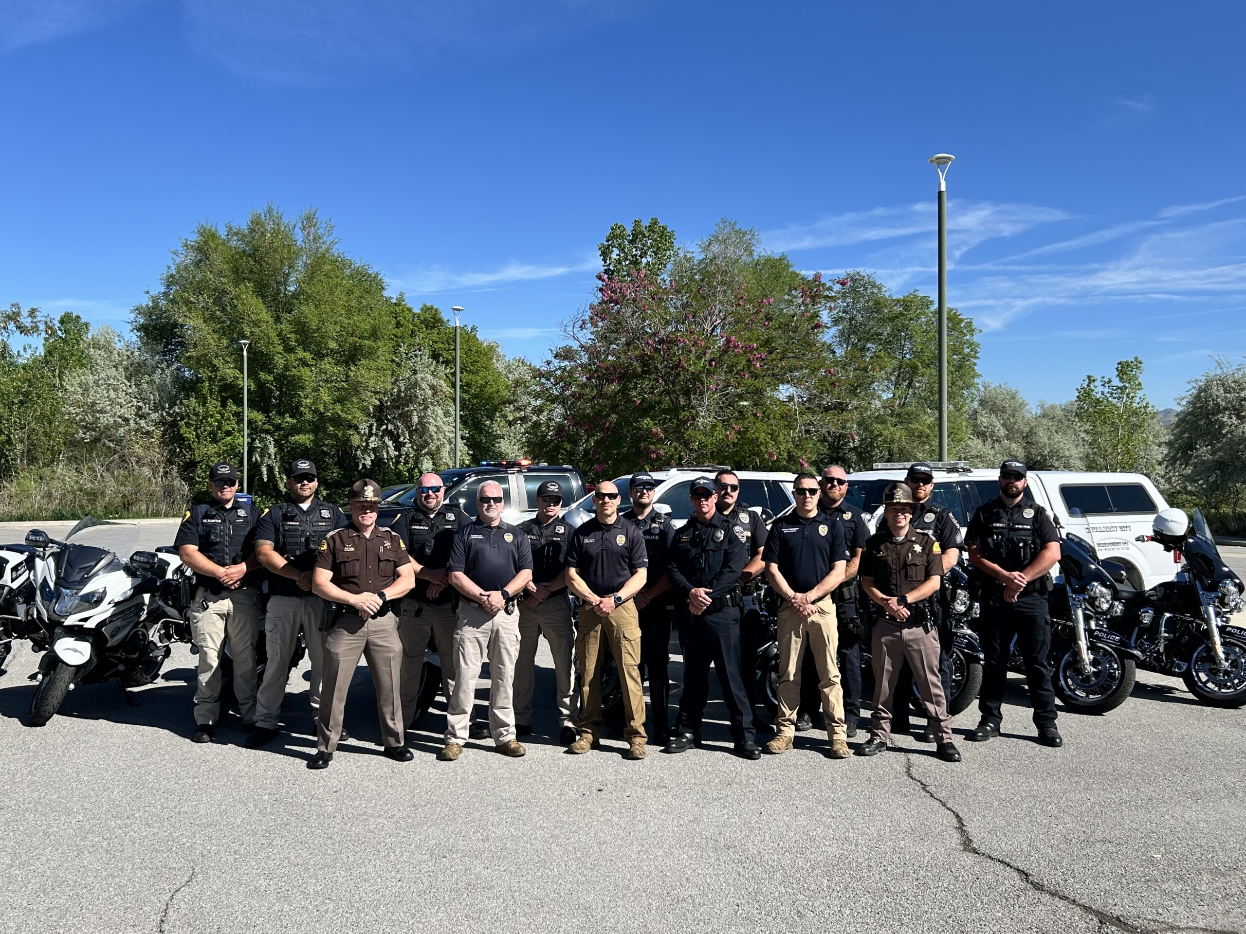 Officers from multiple agencies stand in front of their vehicles